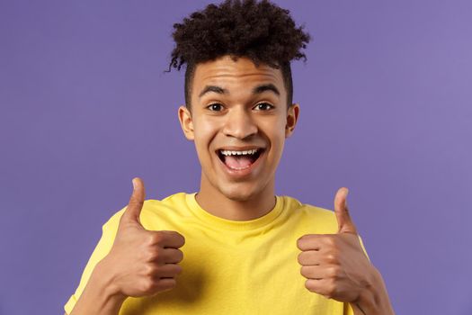 Close-up portrait of enthusiastic, lively hipster guy with afro haircut agree with something, show thumbs-up smiling with joy, recommend good product, like and approve plan, purple background.