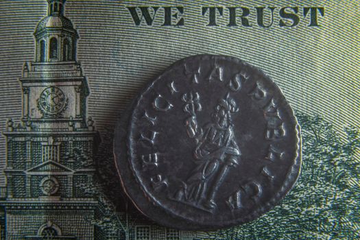 An old Roman coin lies on a 100 dollar bill near the badge with an eagle