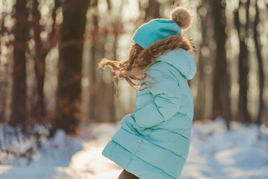 girl in a jacket and hat of turquoise color against the backdrop of a snowy forest