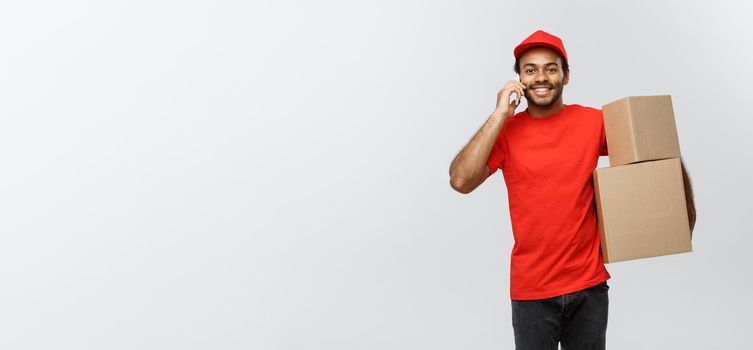 Delivery Concept - Portrait of Handsome African American delivery man or courier with box calling phone to customer. Isolated on Grey studio Background. Copy Space