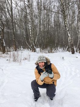 Smiling man with camera in winter forest. Photographer takes pictures of trees under snow. Leisure activity in cold season.
