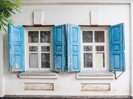 Old building with blue shutters on windows and old fashioned tulle curtains. White stone walls with retro architectural details.