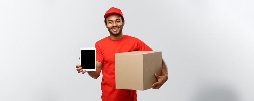 Delivery Concept - Portrait of Handsome African American delivery man or courier with box showing tablet on you to check the order. Isolated on Grey studio Background. Copy Space