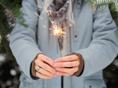 Woman celebrates Christmas or New Year with bright sparkler. Bengal fire, traditional firework for winter holiday celebration outdoors.
