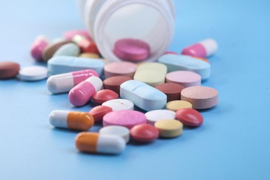 selective focus. close up of colorful pills spilling on blue background .