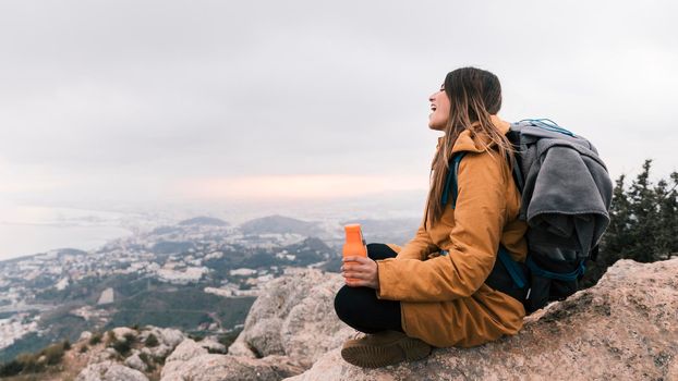 female hiker sitting top mountain holding water bottle hand overlooking view