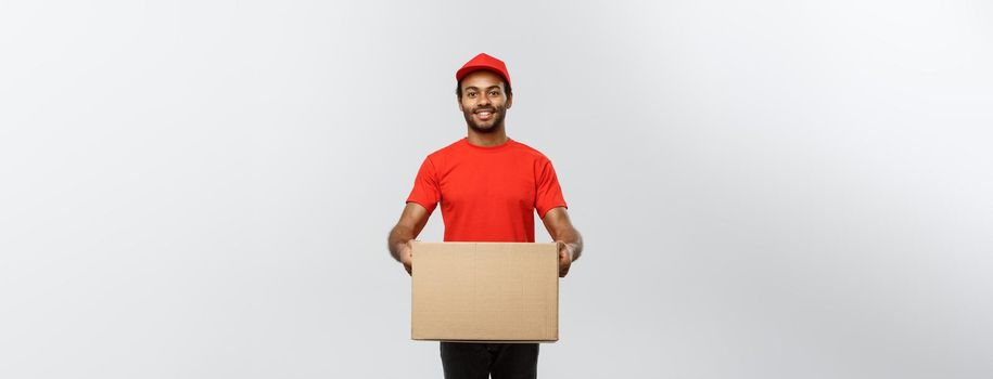 Delivery Concept - Portrait of Happy African American delivery man in red cloth holding a box package. Isolated on Grey studio Background. Copy Space