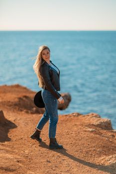 A blonde in a stylish black leather jacket walks along the seashore