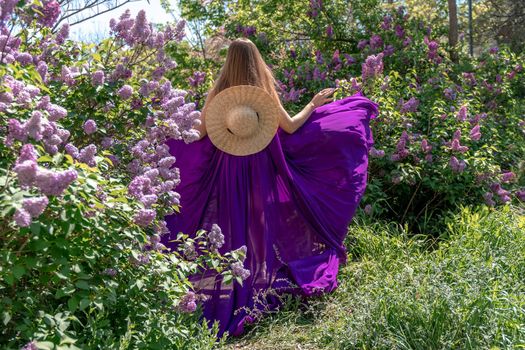 Fashion Model in Lilac Flowers, Young Woman in Beautiful Long Dress Waving on Wind, Outdoor Beauty Portrait in Blooming Garden.