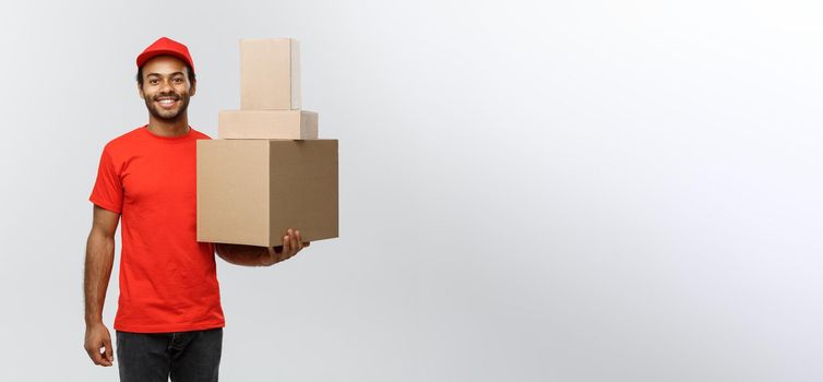 Delivery Concept - Portrait of Happy African American delivery man in red cloth holding a box package. Isolated on Grey studio Background. Copy Space