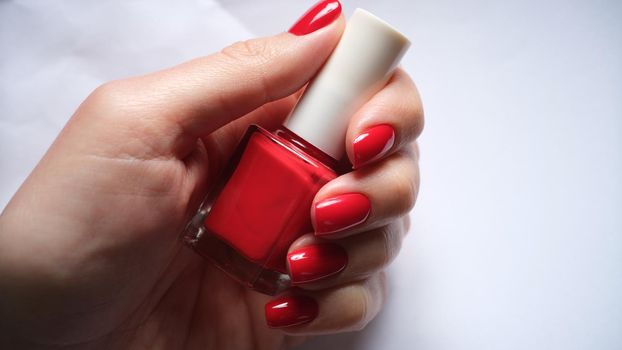 Female nails holds bottle of bright red nail polish. Beautiful manicure concept