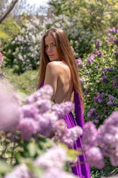 portrait of young woman with long hair outdoors in blooming lilac garden.