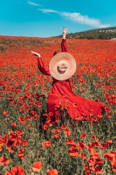 Young woman stands with her back in a long red dress and hat, posing on a large field of red poppies.