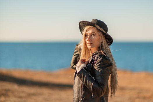 A blonde in a stylish black leather jacket walks along the seashore