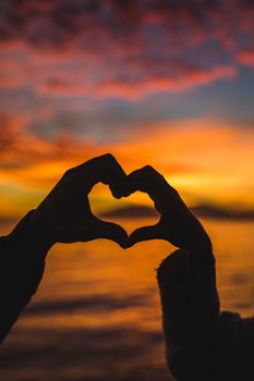 couple making heart from hands sea shore