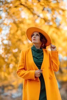 Beautiful woman walks outdoors in autumn. She is wearing a yellow coat, yellow hat and green dress. Young woman enjoying the autumn weather. Autumn content.