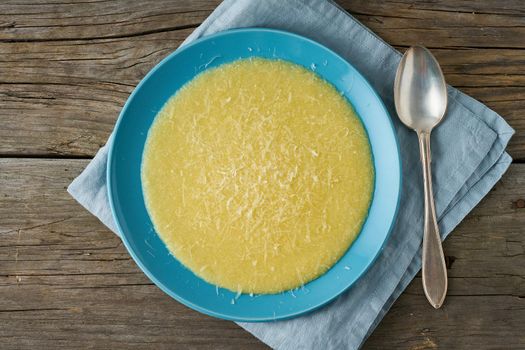 Polenta, porridge with Parmesan cheese on old dark wooden background, top view, traditional Italian cuisine