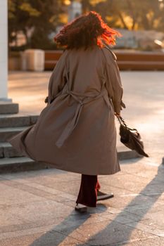 Outdoor fashion portrait of young elegant fashionable brunette woman, model in stylish hat, choker and light raincoat posing at sunset in European city