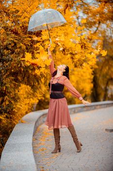 Beautiful girl in a dress with an umbrella in the autumn park. She holds him over her head, autumn leaves are falling out of him.