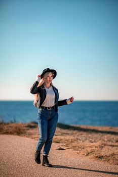 A blonde in a stylish black leather jacket walks along the seashore