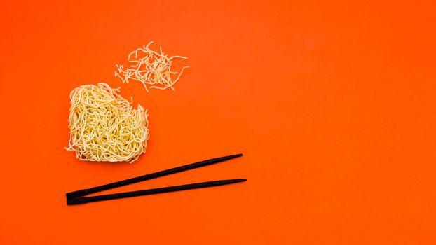 broken dry instant noodles with chopsticks orange background