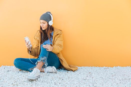 woman sitting rug using smartphone listening music headphones