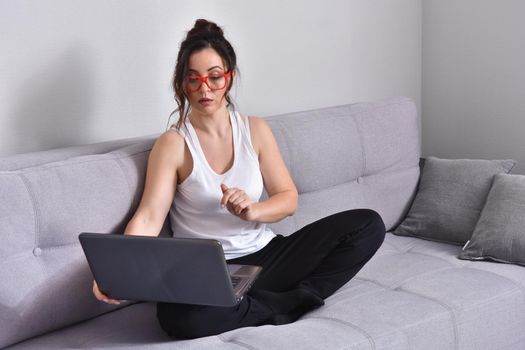 Beautiful brunette woman in red glasses on sofa using laptop