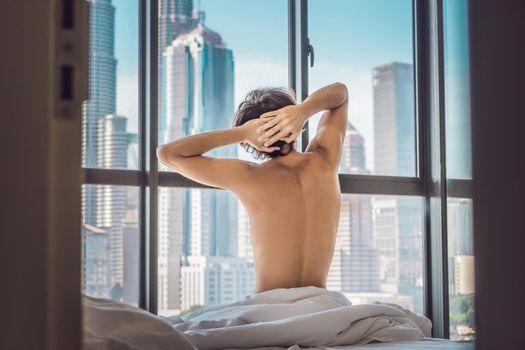 Man wakes up in the morning in an apartment in the downtown area with a view of the skyscrapers. Life in the noise of the big city concept. Not enough sleep.