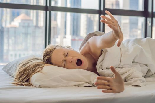 Woman wakes up in the morning in an apartment in the downtown area with a view of the skyscrapers. Life in the noise of the big city concept. Not enough sleep.