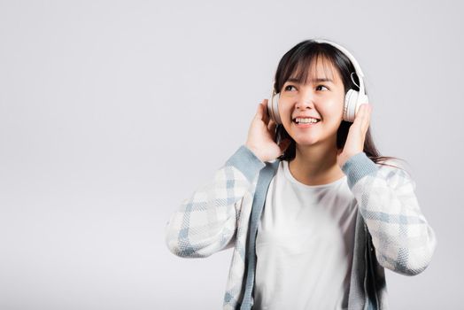 Woman excited smiling listening to music radio in bluetooth headphones and holding phone studio shot isolated white background, happy Asian young female listen modern technology mobile phone