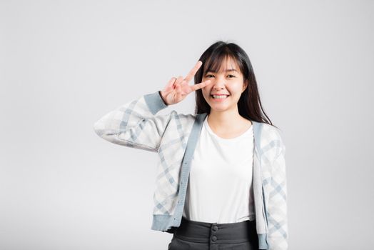 Woman showing finger making v-sign victory symbol near eye looking to camera, Happy Asian beautiful young female mark peace gesture symbol, studio shot isolated on white background with copy space