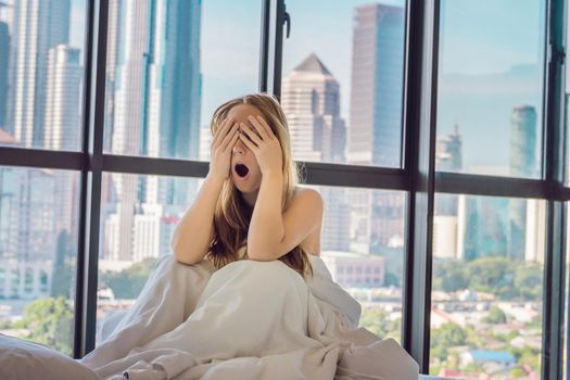 Woman wakes up in the morning in an apartment in the downtown area with a view of the skyscrapers. Life in the noise of the big city concept. Not enough sleep.