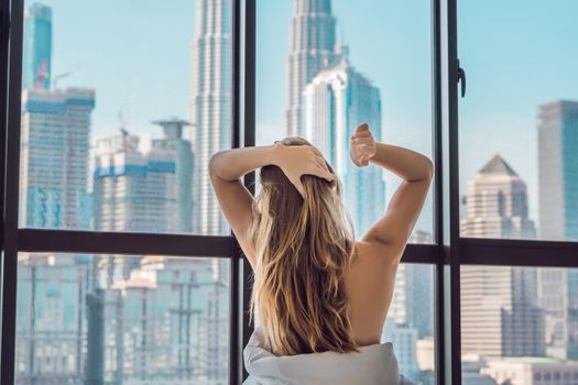 Woman wakes up in the morning in an apartment in the downtown area with a view of the skyscrapers. Life in the noise of the big city concept. Not enough sleep.