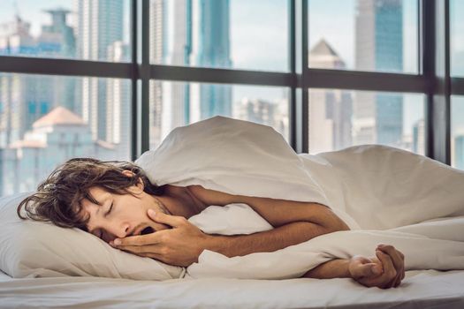 Man wakes up in the morning in an apartment in the downtown area with a view of the skyscrapers. Life in the noise of the big city concept. Not enough sleep.