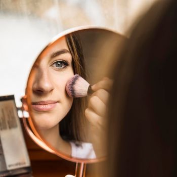 hand mirror with reflection woman applying blusher her face