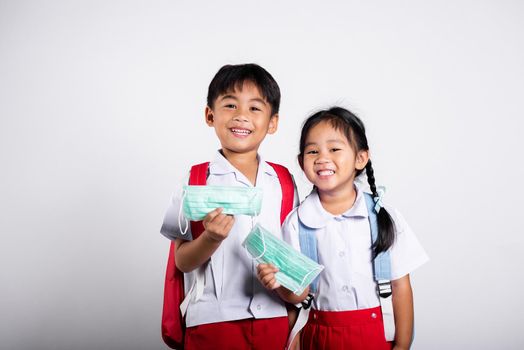 Two Asian student kid girl boy brother sister wearing student thai uniform holding protect mask ready to go to school in studio shot isolated on white background, new normal back to school