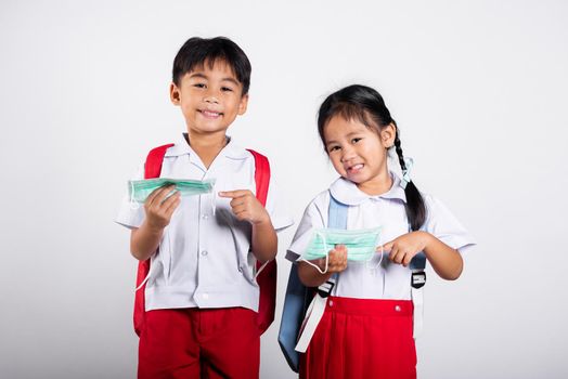 Two Asian student kid girl boy brother sister wearing student thai uniform holding protect mask ready to go to school in studio shot isolated on white background, new normal back to school