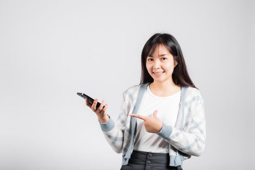 Woman excited celebrating win yes, great news on smartphone she pointing finger to mobile phone studio shot isolated white background, young female smiling having success after received promotion