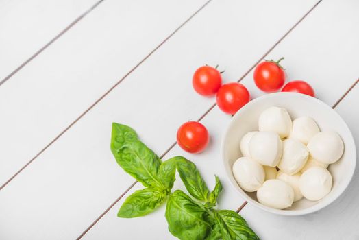 mozzarella cheese ball with basil leaf red tomatoes wooden white background
