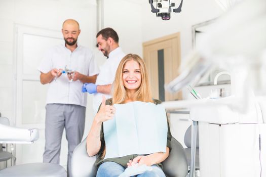 smiling female patient gesturing ok sign front two male dentist