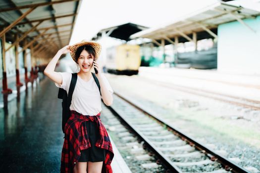 summer, relax, vacation, travel, portrait of beautiful Asian girl using the smartphone mobile to call friends at the train station while waiting for their travel time
