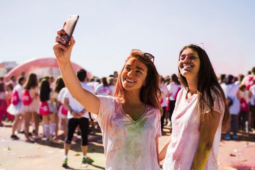 portrait happy young women taking selfie mobile phone during holi festival