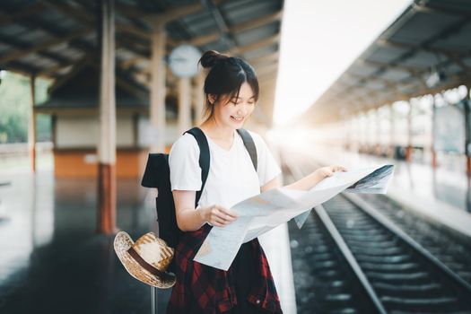 summer, relax, vacation, travel, portrait of a cute Asian girl looking at a map to plan a trip while waiting at the train station