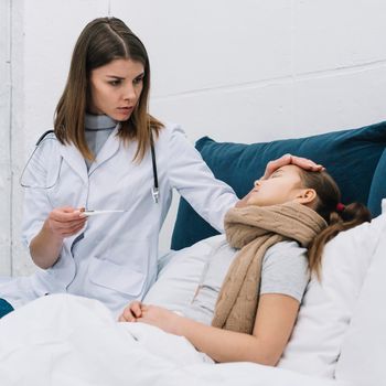 female doctor measuring temperature her sick patient lying bed