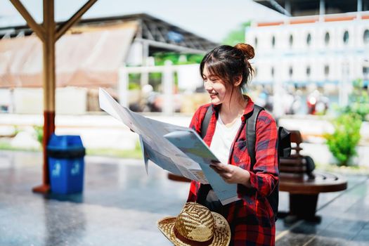 summer, relax, vacation, travel, portrait of a cute Asian girl looking at a map to plan a trip while waiting at the train station