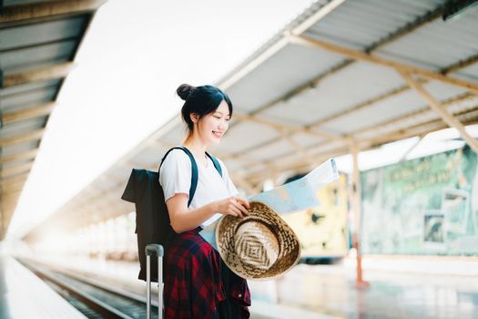 summer, relax, vacation, travel, portrait of a cute Asian girl looking at a map to plan a trip while waiting at the train station