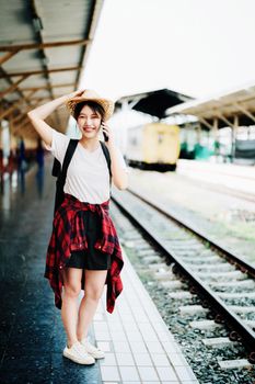 summer, relax, vacation, travel, portrait of beautiful Asian girl using the smartphone mobile to call friends at the train station while waiting for their travel time