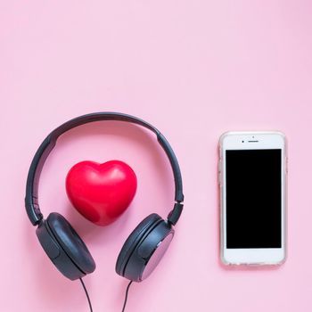 headphone around red heart shape smartphone against pink backdrop