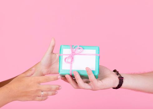 man s hand giving gift box other person against pink background