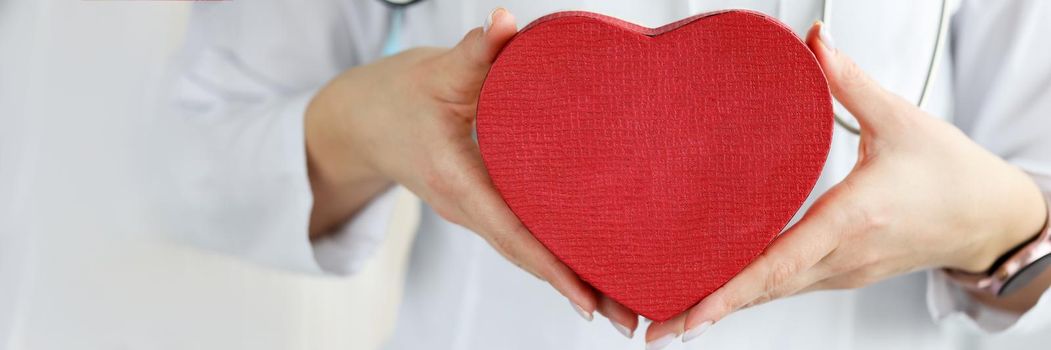 Doctor holding red toy heart in clinic closeup. Diagnosis and treatment of diseases of the cardiovascular system concept